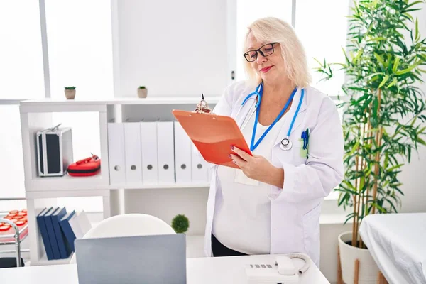 Medelålders Blond Kvinna Bär Läkare Uniform Skriva Dokument Kliniken — Stockfoto