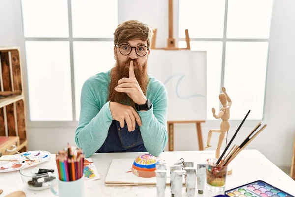 在艺术工作室里 红头发的男人留着长胡子 画着黏土碗 要求安静 手指放在嘴唇上 沉默和秘密概念 — 图库照片