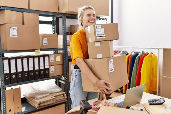 Young blonde woman working at small business ecommerce smiling and laughing hard out loud because funny crazy joke.