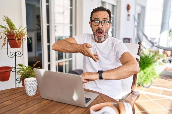 Middle age man using computer laptop at home in hurry pointing to watch time, impatience, upset and angry for deadline delay