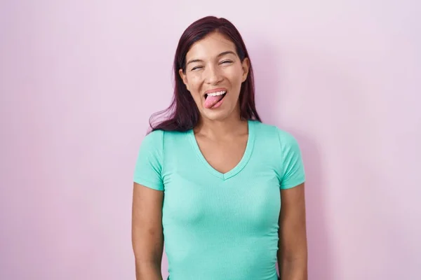 ピンク色の背景に立っている若いヒスパニック系の女性が面白い表情で幸せ舌を突き出しています 感情の概念 — ストック写真