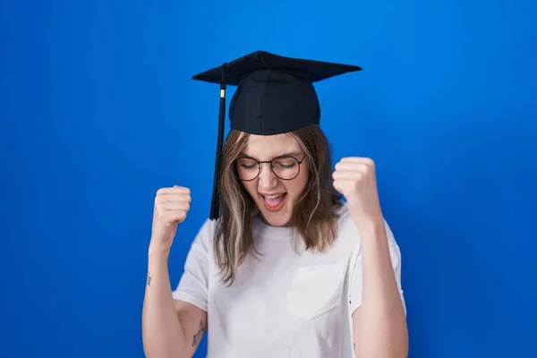 金发的高加索女人戴着毕业典礼帽 高兴而兴奋地举起双臂做着获胜的手势 微笑着 尖叫着要成功 庆祝概念 — 图库照片
