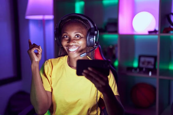 Африканская Американка Играет Видеоигры Смартфоном Улыбаясь Показывая Рукой Пальцем Сторону — стоковое фото