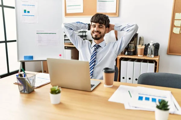 Young hispanic businessman relaxed with hands on head working at the office.
