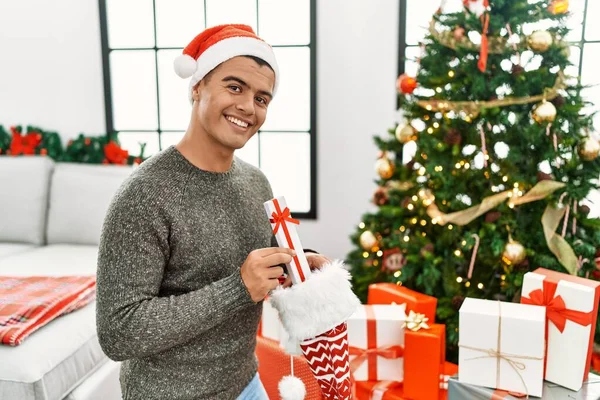 Young Hispanic Man Putting Gifts Christmas Sock Home — Fotografia de Stock