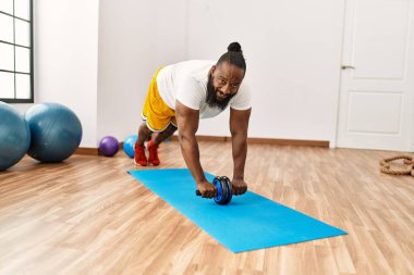 Genç Afrikalı Amerikalı gülümseyen bir adam spor merkezinde paten kullanarak karın kası egzersizi yapıyor.