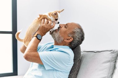 Yaşlı, gri saçlı, gülümseyen ve elinde Chihuahua tutan adam.