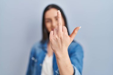 Hispanic woman standing over blue background showing middle finger, impolite and rude fuck off expression 