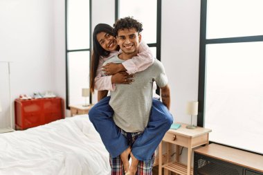Yatak odasında mutlu bir şekilde gülümseyen genç Latin çift. Kadını sırtında taşıyan bir adam.