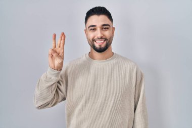 Young handsome man standing over isolated background showing and pointing up with fingers number three while smiling confident and happy. 