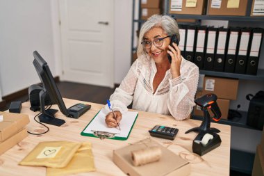 Orta yaşlı kadın ecommerce iş işçisi akıllı telefondan konuşuyor ofisteki panoya yazı yazıyor.