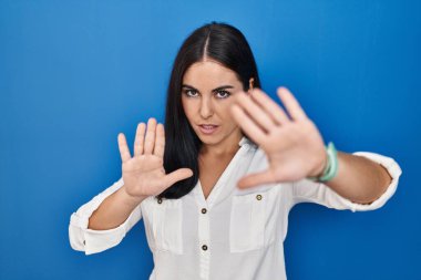 Mavi arka plan üzerinde duran genç İspanyol kadın el ve parmakları kullanarak çerçeve yapıyor, kamera bakış açısı. 