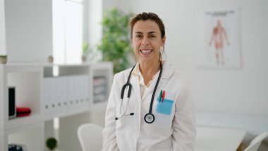 Klinikte dikilen orta yaşlı İspanyol kadın doktor üniforması giyiyor.
