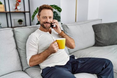 Orta yaşlı İspanyol adam akıllı telefonla konuşuyor evde kahve içiyor.