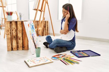 Resim stüdyosunda resim çizen şüpheyle bakan genç Latin kadın.