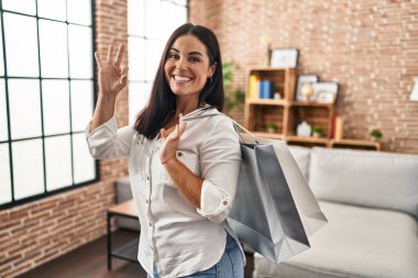 Elinde alışveriş torbaları tutan genç İspanyol kadın parmaklarıyla imza atıyor, gülümseyerek mükemmel bir sembol oluşturuyor. 