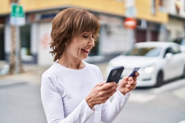 Sokakta akıllı telefon ve kredi kartı kullanan orta yaşlı bir kadın.