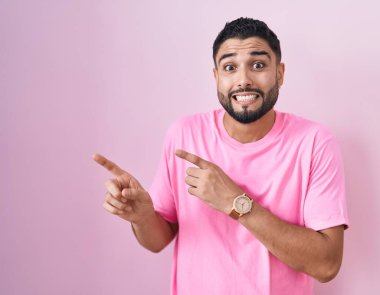 İspanyol genç bir adam pembe arka planda dikiliyor. Endişeli ve gergin olduğunu gösteriyor. Endişeli ve şaşırmış bir ifadeyle. 