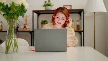 Genç kızıl saçlı kadın evde oturmuş müzik dinliyor.