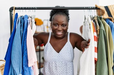 Young african american woman customer appearing throw clothes rack at clothing store