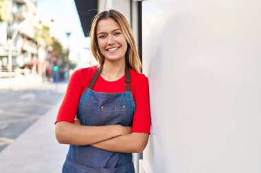 Young hispanic woman shop assistant standing with arms crossed gesture at street