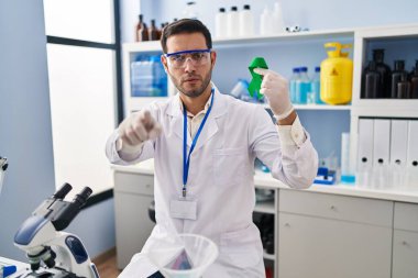 Laboratuvarda çalışan sakallı genç İspanyol bir adam elinde yeşil kurdeleyle kamerayı ve seni işaret ediyor. Kendine güveni tam bir jest. 