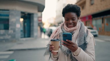 Genç Afrikalı Amerikalı kadın akıllı telefon kullanıyor. Sokakta kahve içiyor.