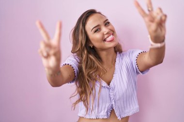 Pembe arka planda dikilmiş, ağzı açık gülümseyen genç İspanyol kadın zafer işareti yapıyor. İki numara.. 