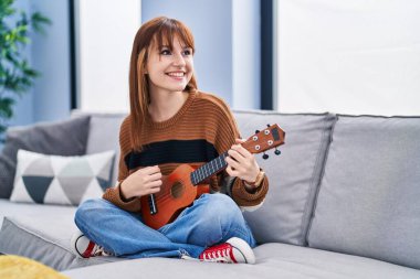 Evdeki koltukta ukelele oynayan genç bir kadın.