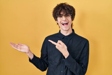 Sarı arka planda gözlük takan genç adam kameraya hayret ediyor ve gülümsüyor.. 