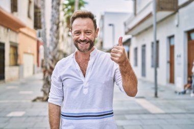 Şehirdeki orta yaşlı adam elleriyle mutlu bir jest yapıyor. Kameraya bakıp başarıyı gösteren ifade. 