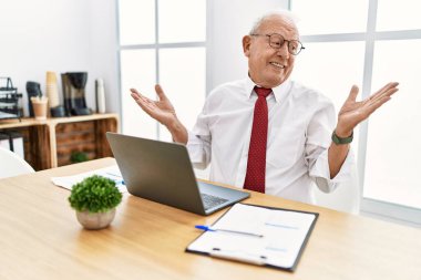 Ofiste çalışan kıdemli bir adam bilgisayarla gülümsüyor. İki elini de açık gösteriyor. Karşılaştırma ve reklam karşılaştırması yapıyor ve dengeyi sağlıyor. 