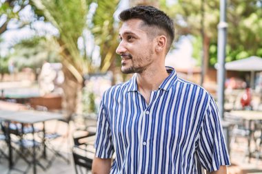 Genç yakışıklı adam parkta kendinden emin gülümsüyor.