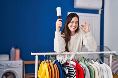 Çamaşırhanede genç esmer bir kadın. Evcil hayvan tüyü temizleyicisiyle giysileri temizliyor. Parmaklarıyla imza atıyor. 