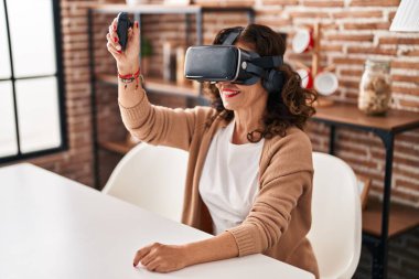 Orta yaşlı İspanyol kadın evde sanal gerçeklik gözlüğü takıyor.