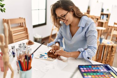 Genç ve güzel İspanyol kadın sanatçı gülümsüyor. Kendine güveni tam. Sanat stüdyosunda elleriyle seramik demlik yapıyor.