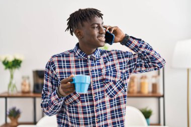 Afro-Amerikalı adam akıllı telefondan konuşuyor evde kahve içiyor.