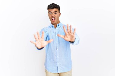 Tecrit edilmiş arka planda duran İspanyol gömlekli genç adam korku ifadesinden korkuyor ve dehşete düşüyor. El hareketlerini durdur, şok içinde bağır. panik konsepti. 