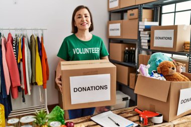 Middle age hispanic woman holding donations box at donations stand