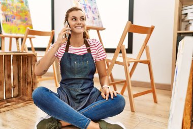 Sanat stüdyosundaki akıllı telefondan konuşan kendine güvenen genç bir kadın.