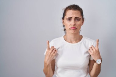 Güzel esmer kadın izole arka planda dikiliyor üzgün ve üzgün görünüyor, parmaklarıyla yön gösteriyor, mutsuz ve depresif.. 