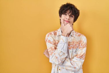 Gündelik tişört giyen genç adam kameraya kendinden emin bakıyor kollarını kavuşturup gülümsüyor ve elini çenesine kaldırıyor. Olumlu düşünmek. 