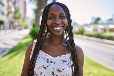 Genç Afrikalı Amerikalı kadın gülümseyerek şehirde mutlu mesut duruyor..