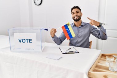 Siyasi seçim kampanyasında sakallı genç yakışıklı adam elinde Venezuela bayrağı ile mutlu ve gururlu bir gülümsemeyi işaret ediyor. 