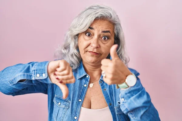 ピンクを背景に白髪の中年女性が親指を上下に 意見の相違や合意表現を行う 狂気の葛藤 — ストック写真