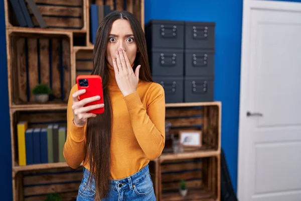 Genç esmer kadın akıllı telefon kullanarak ağzını eliyle kapatıyor, şok geçiriyor ve hata yapmaktan korkuyor. şaşırmış ifade  