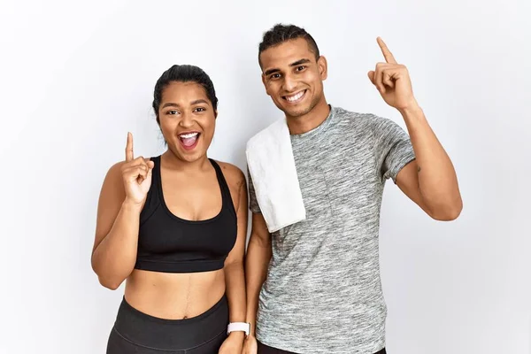 İzole edilmiş arka planda spor kıyafetleri giyen genç latin çift başarılı bir fikir sunuyor. Heyecanlı ve mutlu. Bir numara.. 