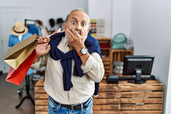 Butik dükkanında alışveriş poşetleri tutan yakışıklı bir adam yanlışlıkla ağzı ellerle kapatırken şok oldu. gizli kavram. 