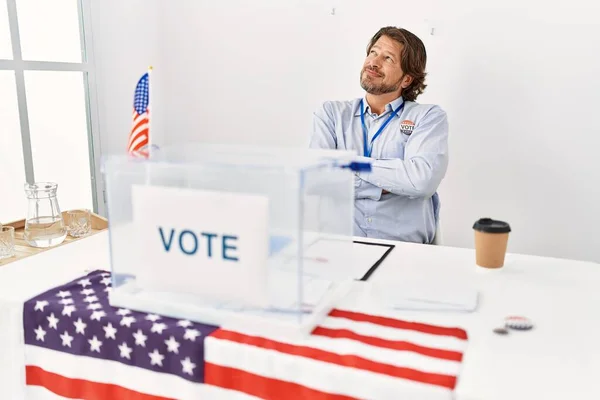 一个英俊的中年男人坐在投票站里 面带微笑地看着旁边 目不转睛地想着 — 图库照片