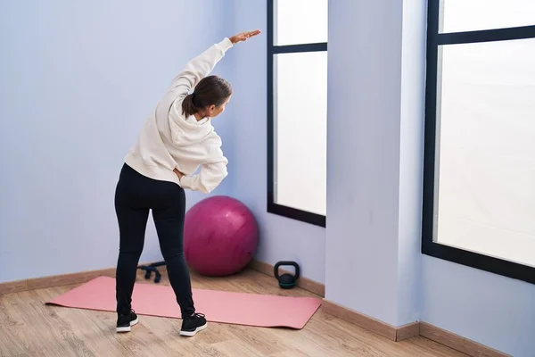 Middle age woman stretching standing on back view at sport center